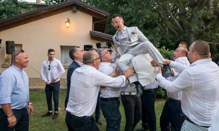 Frame di uno sposo che viene sollevato con sedia da amici