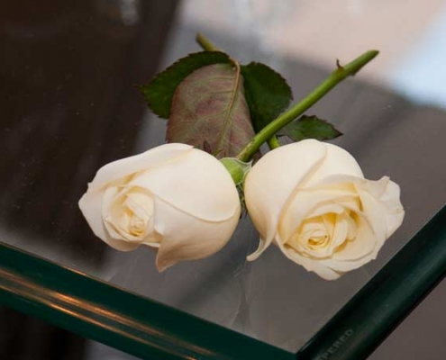 Servizio-fotografico-matrimonio-low-cost-due rose gialle incrociate poste su di un tavolo in cristallo