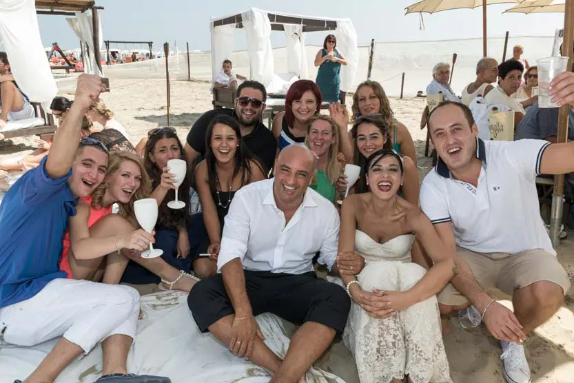Immagine di matrimonio gruppo con sposi seduti sulla spiaggia