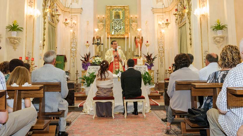 Cerimonia religiosa sposi di spalle con sacerdote che predica