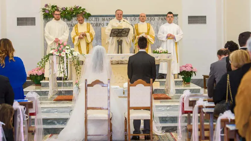 Sposi di spalle in Chiesa che ascoltano il sacerdote