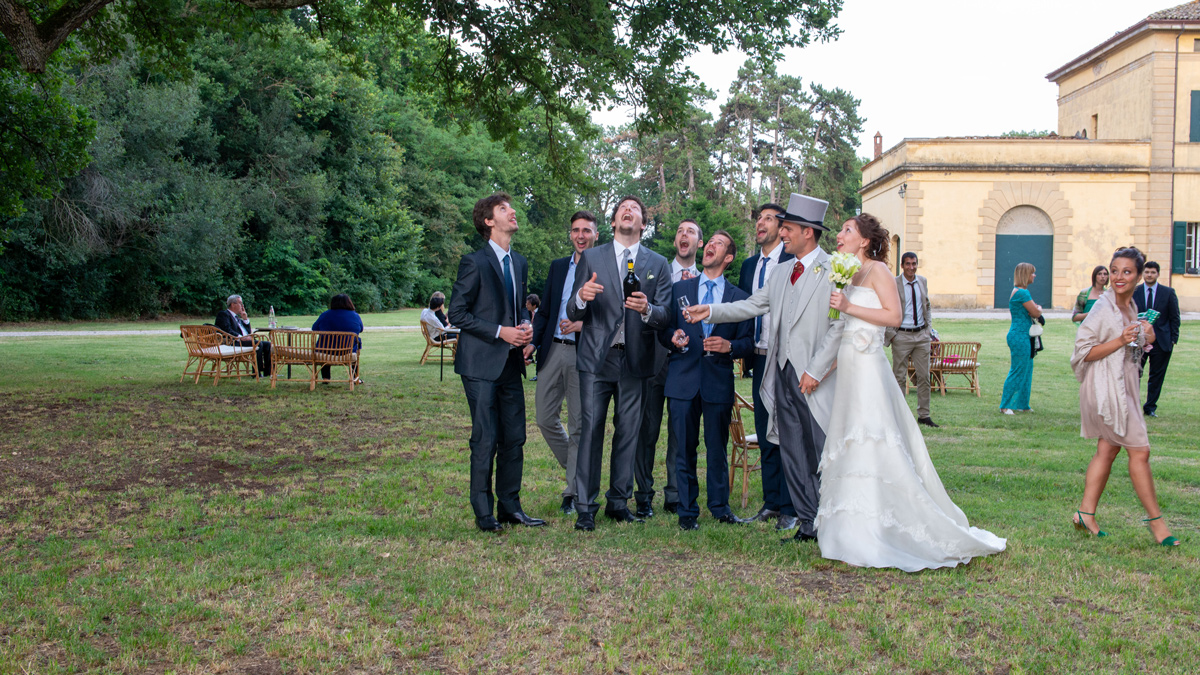 Sposo stappa lo spumante mentre gli invitati guardano in alto nel parco di Villa Isolani a Ozzano dell'Emilia