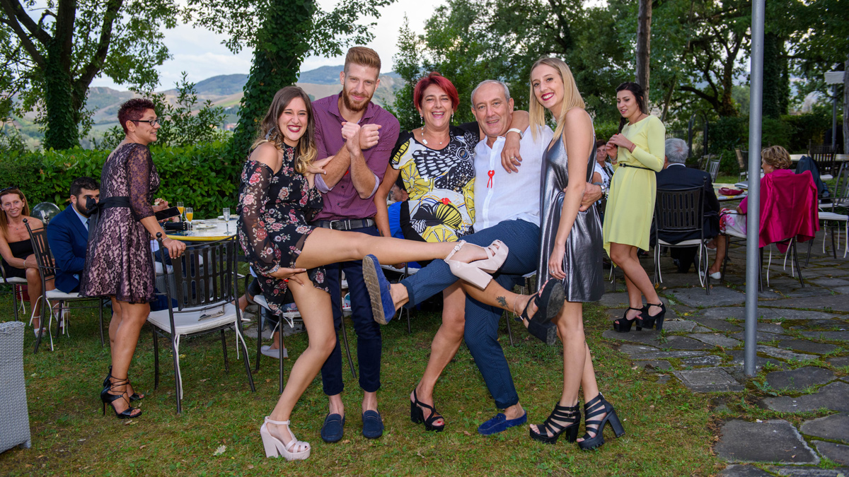 Gruppo di invitati in posa scherzosa nel giardino di Villa Montrona, con le colline di Imola sullo sfondo durante il ricevimento di matrimonio