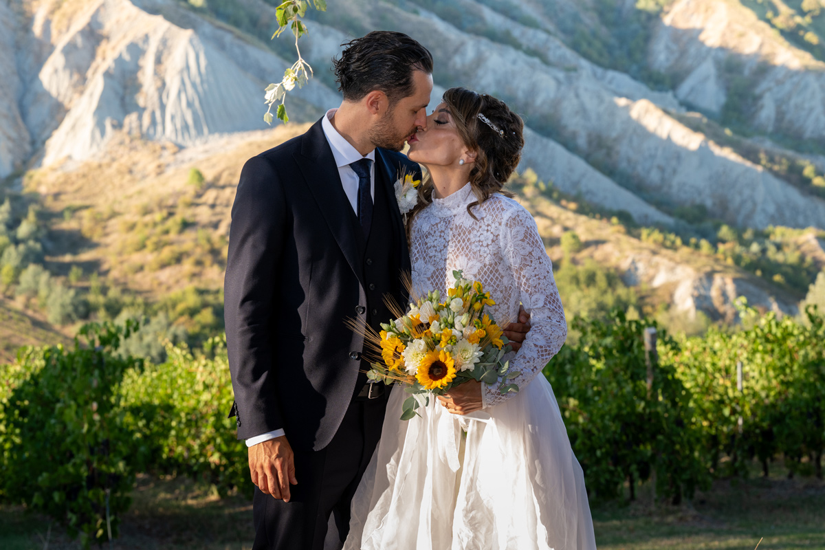 Preventivo fotografo matrimonio: bacio degli sposi con vigneto e calanchi sullo sfondo