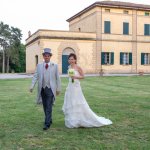 Villa Isolana, sposo in marsina e sposa con bouquet camminano sul prato con la villa sullo sfondo
