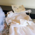 Vestito da sposa steso su letto con cartello di carta che simola viso